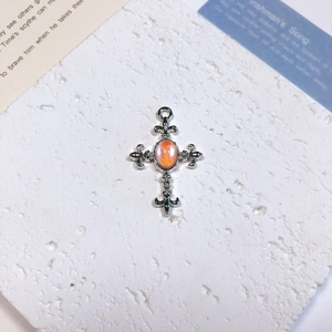 Macro shot of silver cross pendant with orange opal stone on a white textured stone base