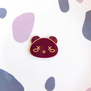 Detail of a dark red panda enamel pin with golden metallic edges and cute cartoon design