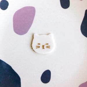 Détail d'une breloque chat en acrylique blanc avec traits et moustaches peints en or