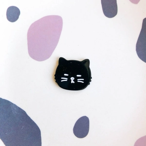 Détail d'un badge en émail chat noir mignon avec lignes blanches et finition brillante