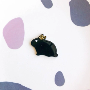Detail view of cute black rabbit enamel pin with gold accents on a patterned background