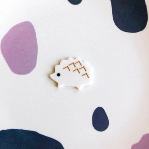 Detail of a cute white acrylic hedgehog accessory with golden spike patterns and black eyes