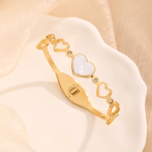 Gold hollow heart bangle with white shell inlay and zircon accents on silk background