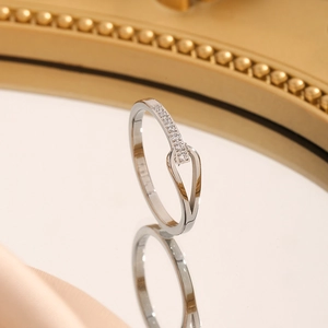 Detailansicht eines silbernen Kreuzrings mit Pavé-Diamanten auf einer Spiegelfläche