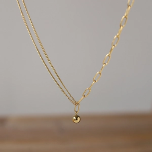 Collana dorata asimmetrica con maglie a graffetta e un ciondolo a sfera lucido