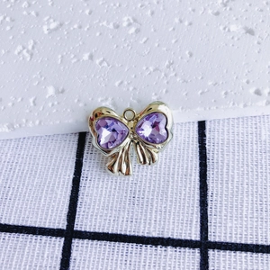 Close-up of golden bow pendant with purple heart-shaped cubic zirconia inlay