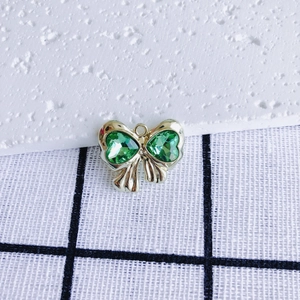 Detailed view of a gold bow pendant with green heart-shaped crystal zircon inlay