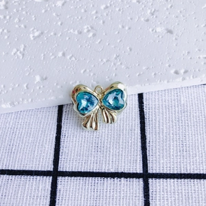 Detail view of a gold bow pendant with blue heart-shaped gems and metallic textures