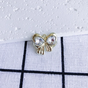 Macro detail of golden bow charm with heart-shaped zircon inlays for jewelry making