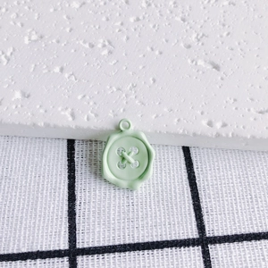 Macro detail of mint green alloy button pendant with wax seal texture and top loop