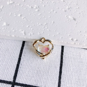 Close-up of golden heart pendant with iridescent pink stone and small white pearl detail