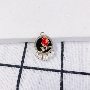 Nahaufnahme von Rosenanhänger mit roter Blüte, Glitzerrahmen und fünf weißen Perlen