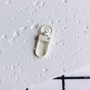 Gros plan d'un fermoir mousqueton en métal blanc mat avec crochet pivotant en anneau D