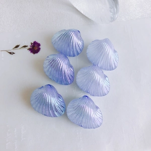 Close-up of iridescent fan-shaped shell charms in blue-purple for DIY jewelry making
