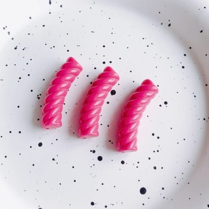 Primo piano di tre perline a spirale in resina magenta per gioielli fai-da-te su un piatto
