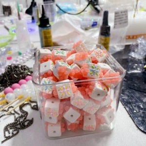 Macro view of white square DIY beads with floral patterns and pink textured frosted grains