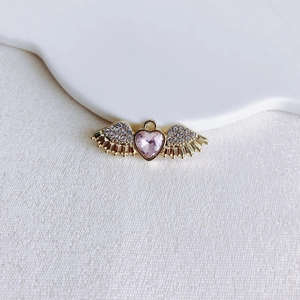 Detail of a golden angel wing heart pendant with pink gemstone and pavé rhinestones