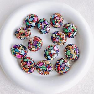Macro view of twelve colorful mosaic oval beads with rhinestones in a white ceramic tray