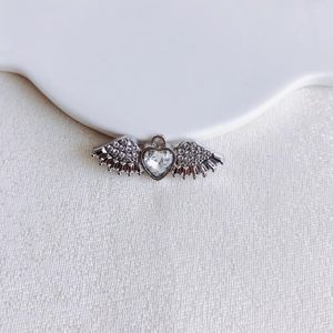 Macro detail of silver heart pendant with crystal wings and polished metal texture