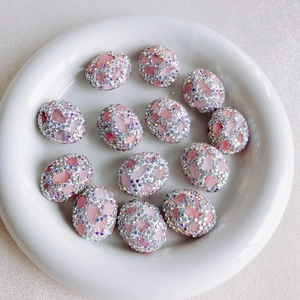 Close-up of pink crystal rhinestone-encrusted oval beads on white ceramic tray