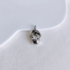 Detail shot of a liquid-style irregular silver pendant on a white ceramic plate