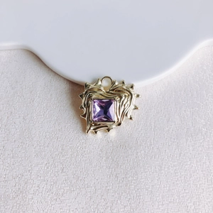 Macro detail of heart pendant with lava texture and purple gemstone in gold finish