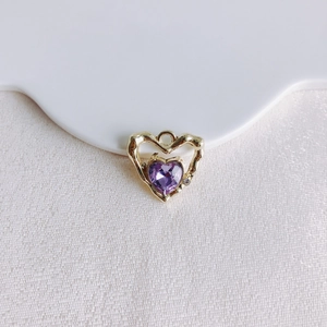 Détail d'un pendentif cœur en pierre violette avec bord doré ondulé et petite pierre