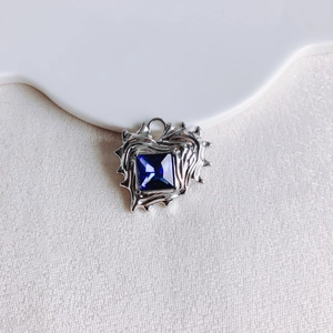 Macro detail of irregular silver heart pendant with square blue zircon on fabric