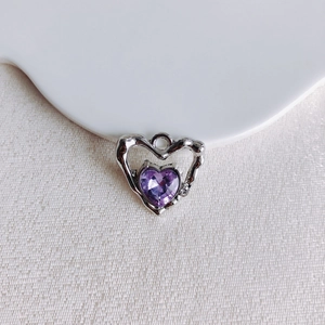 Gros plan d'un pendentif cœur argenté avec pierre précieuse violette sur tissu blanc