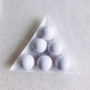 Detailed view of six glossy white acrylic round beads arranged in a white triangle tray