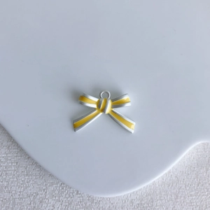 Detailed view of yellow bow-knot alloy pendant on a white ceramic plate for DIY jewelry