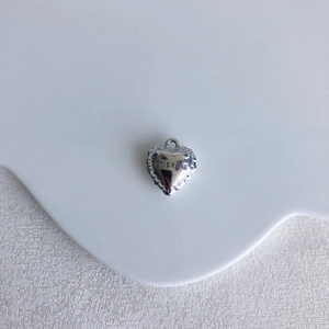 Detailed close-up of a silver heart charm featuring SWEETIE engraving and scalloped edges