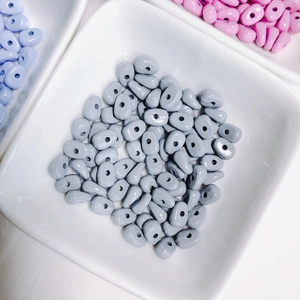 Flat oval spray-painted alloy beads in Morandi colors displayed on a white ceramic plate