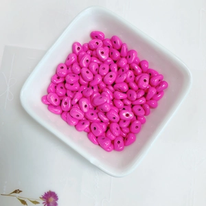 Macro detail of glossy magenta spray-painted alloy beads with holes in a ceramic bowl