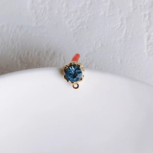 Macro detail of a blue crystal earring stud with a gold floral petal setting