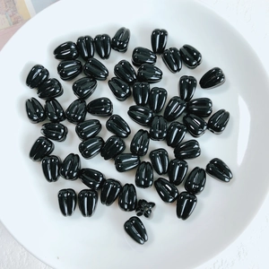 Macro shot of black teardrop-shaped acrylic beads with longitudinal textures in a white dish