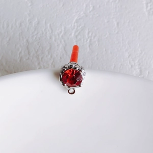 Macro view of silver four-prong setting with a ruby-red zircon pendant and connector loop