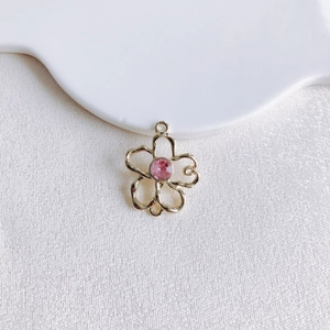 Vue détaillée d'un pendentif fleur dorée avec zircon rose et pétales ajourés