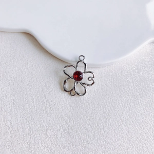 Détail d'un pendentif fleur en argent avec pétales évidés et cristal rouge central