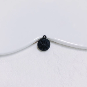 Vue détaillée d'un pendentif rond noir mat avec gravure d'étoile radiale sur un plateau blanc
