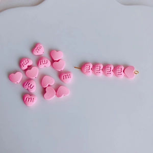 Nahaufnahme rosa herzförmiger Perlen mit eingravierten Buchstaben für DIY Schmuck