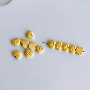Makro-Detail von gelben Herz-Legierungsperlen mit m-Gravur für DIY-Haarschmuck und Bastelbedarf