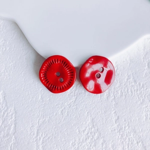 Macro shot of two red flower-shaped resin buttons with radial texture and hammered patterns