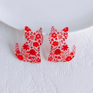 Macro detail of acrylic cat charms with vibrant red floral patterns and hanging holes