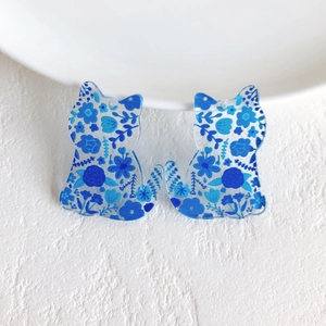 Macro detail of acrylic cat charms featuring intricate blue floral patterns and glossy finish