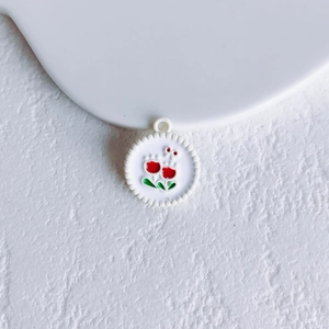 Close-up of a white floral pendant with red flower enamel and metal border for DIY jewelry