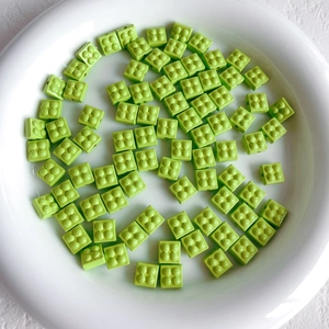 Close-up of grass green building block style loose beads for DIY jewelry in a ceramic bowl
