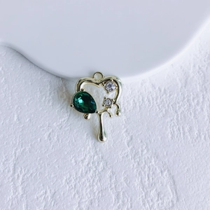 Macro shot of gold heart pendant with pear-shaped green gem and white zircon accents
