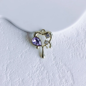 Macro detail of a golden heart pendant with purple teardrop gem and liquid drip effect