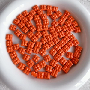 Macro detail of bright orange 2x2 building block beads in a white ceramic dish